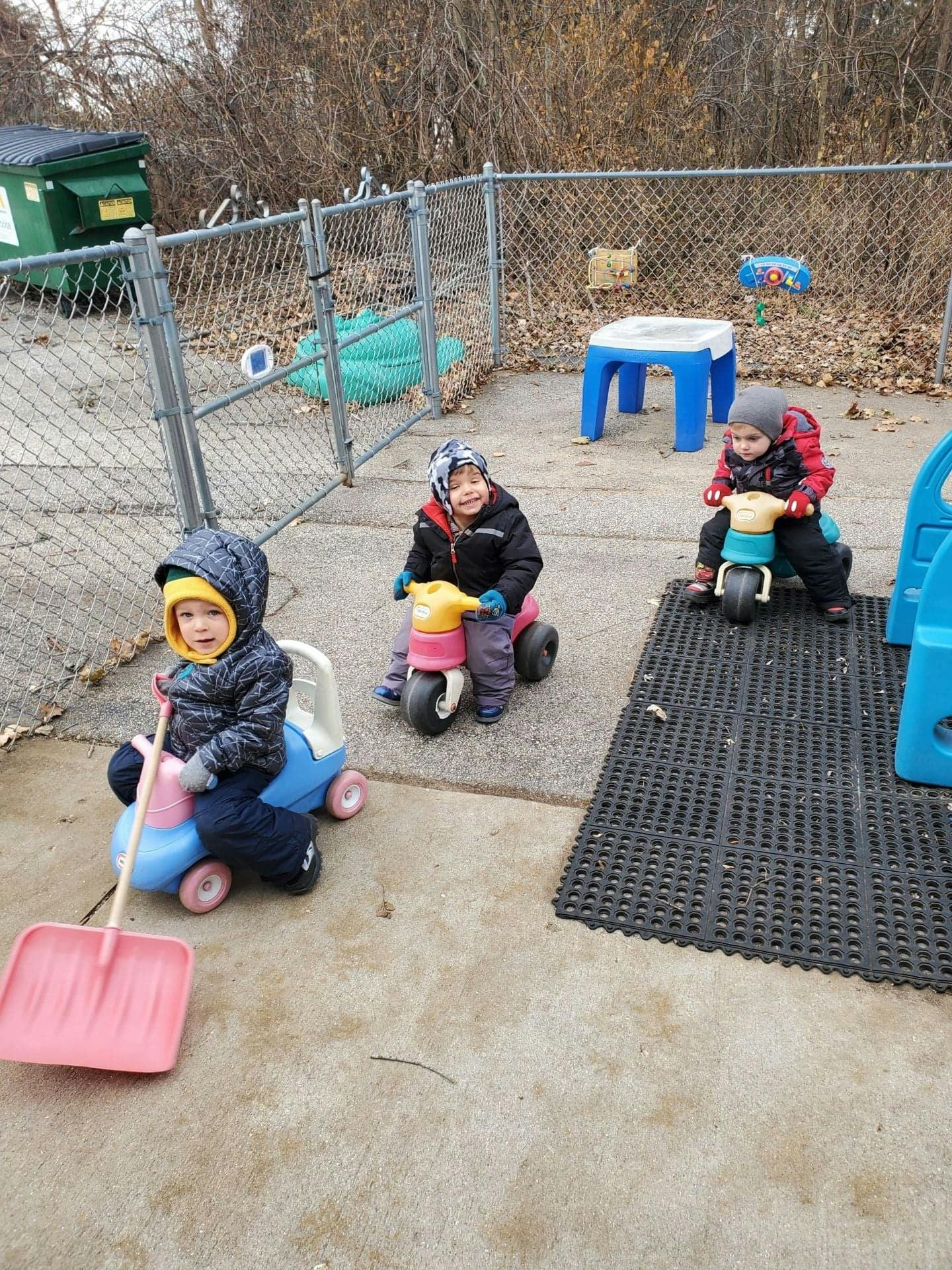 Three children riding toy vehicles outdoors