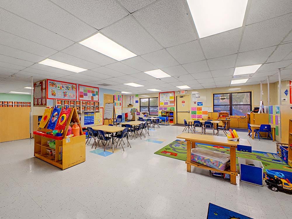 Empty classroom with small tables and chairs, art easel, and play rugs