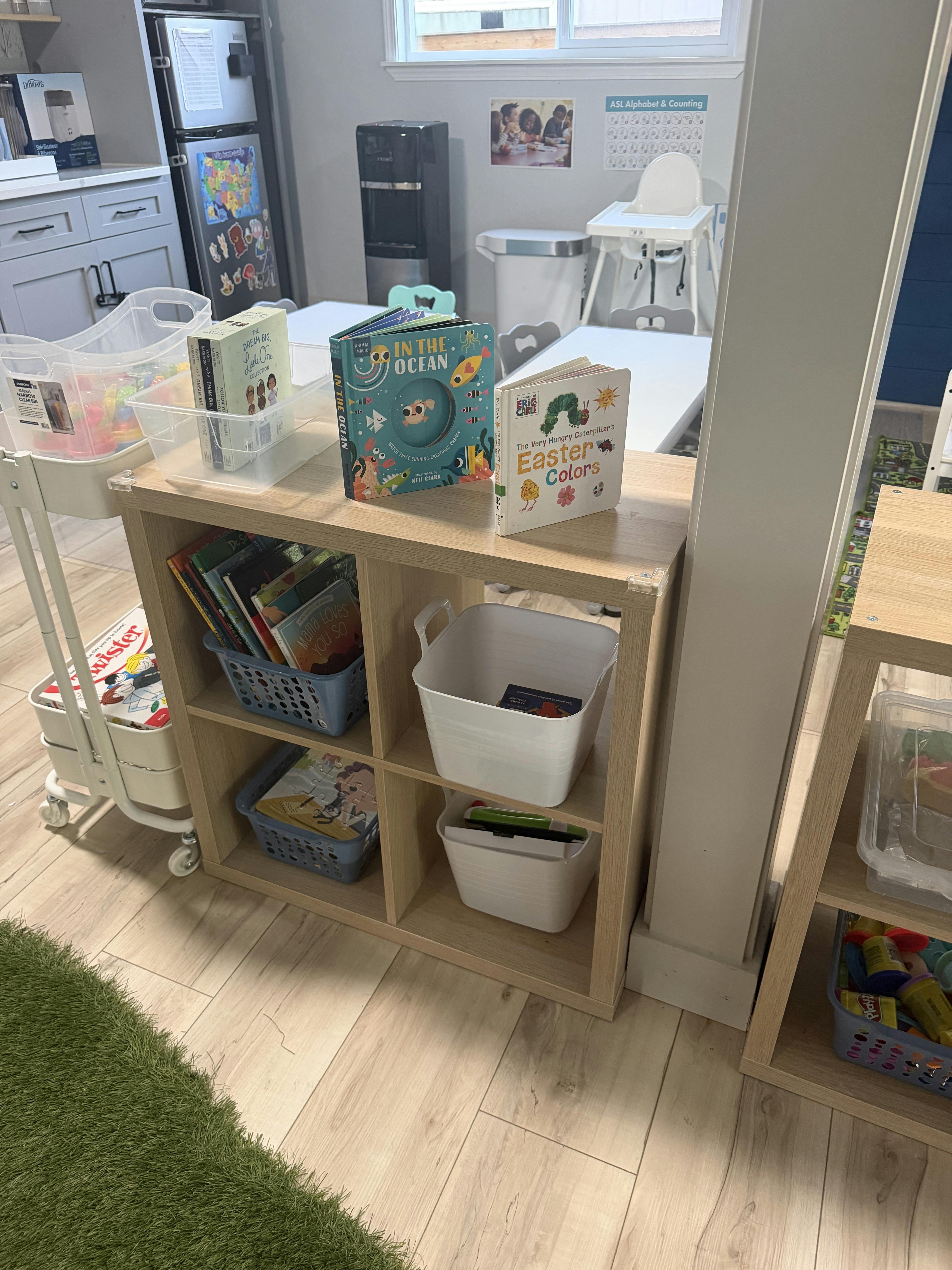 Childrens books and storage bins on a wooden shelf in a classroom
