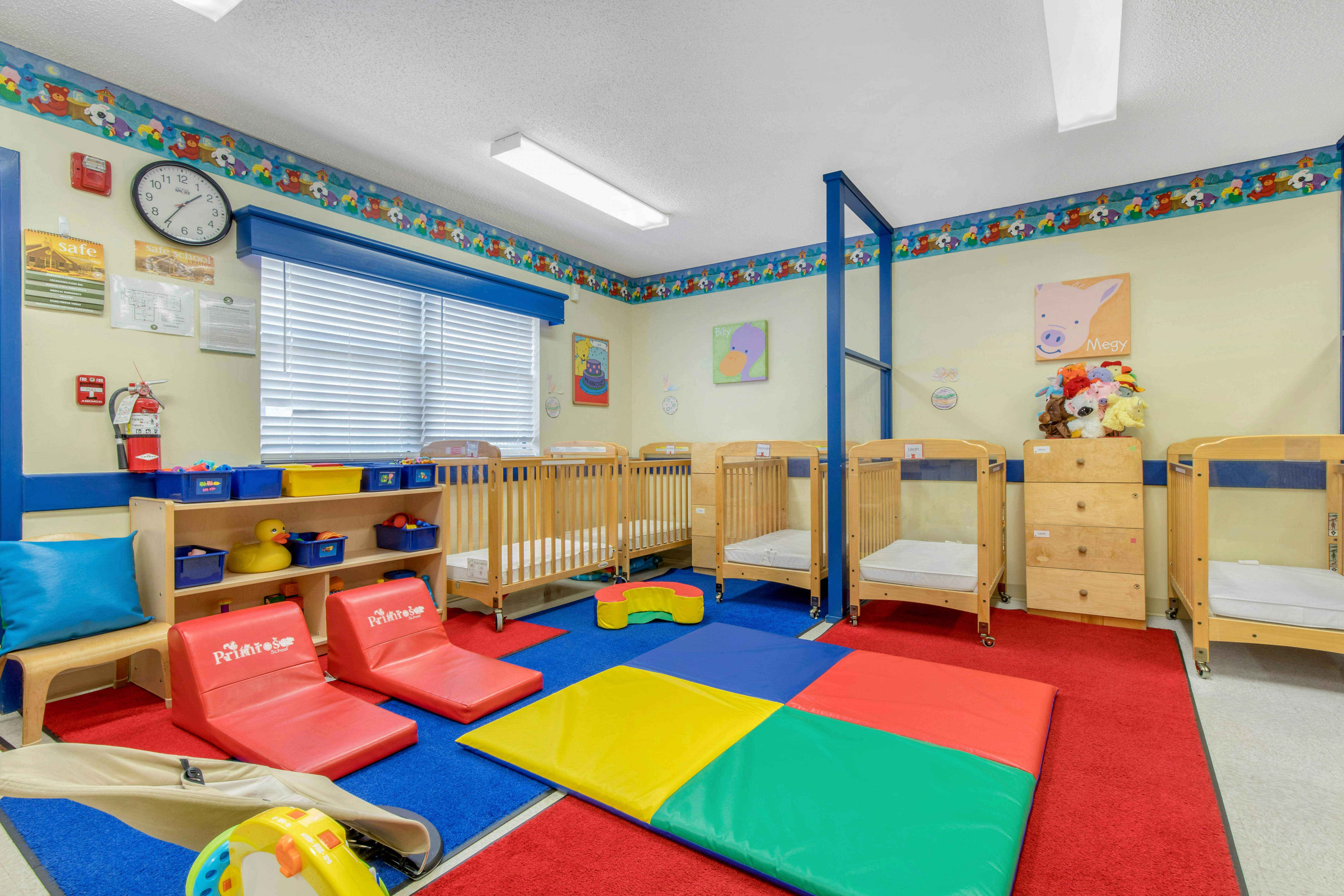 A childcare center classroom with cribs, play mats, and learning materials