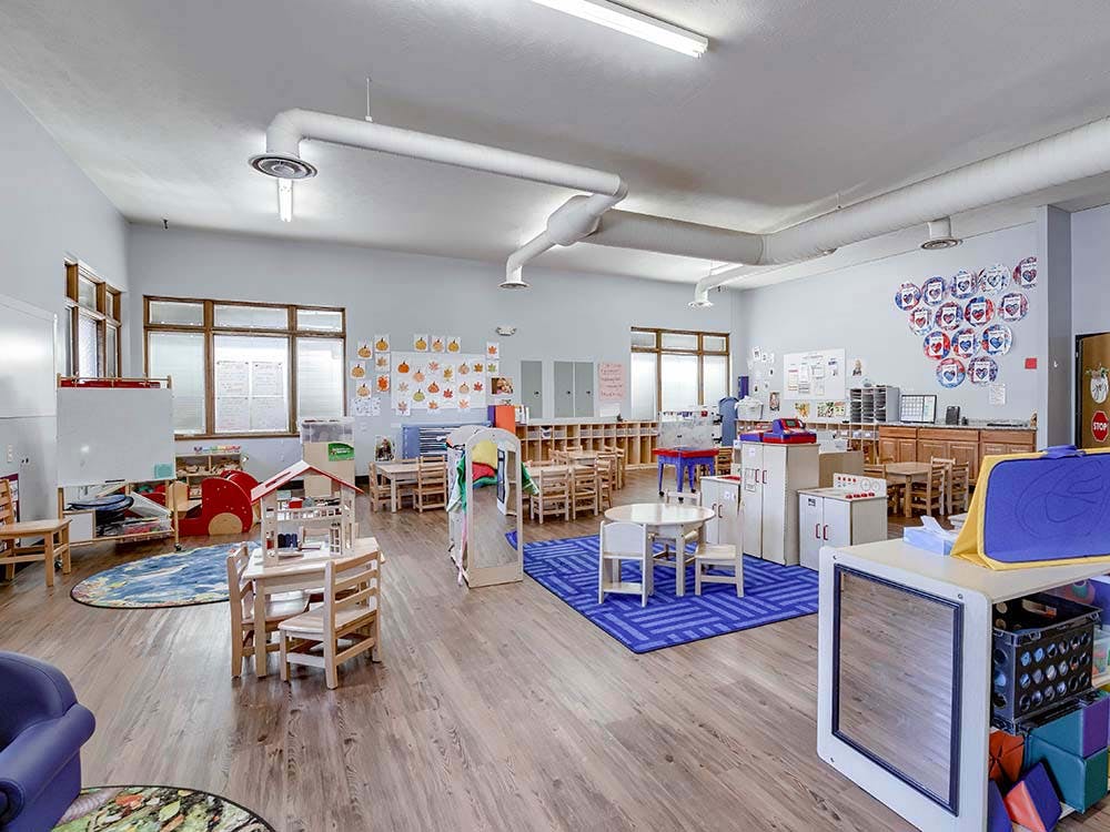 Empty classroom with small tables, chairs, and play areas