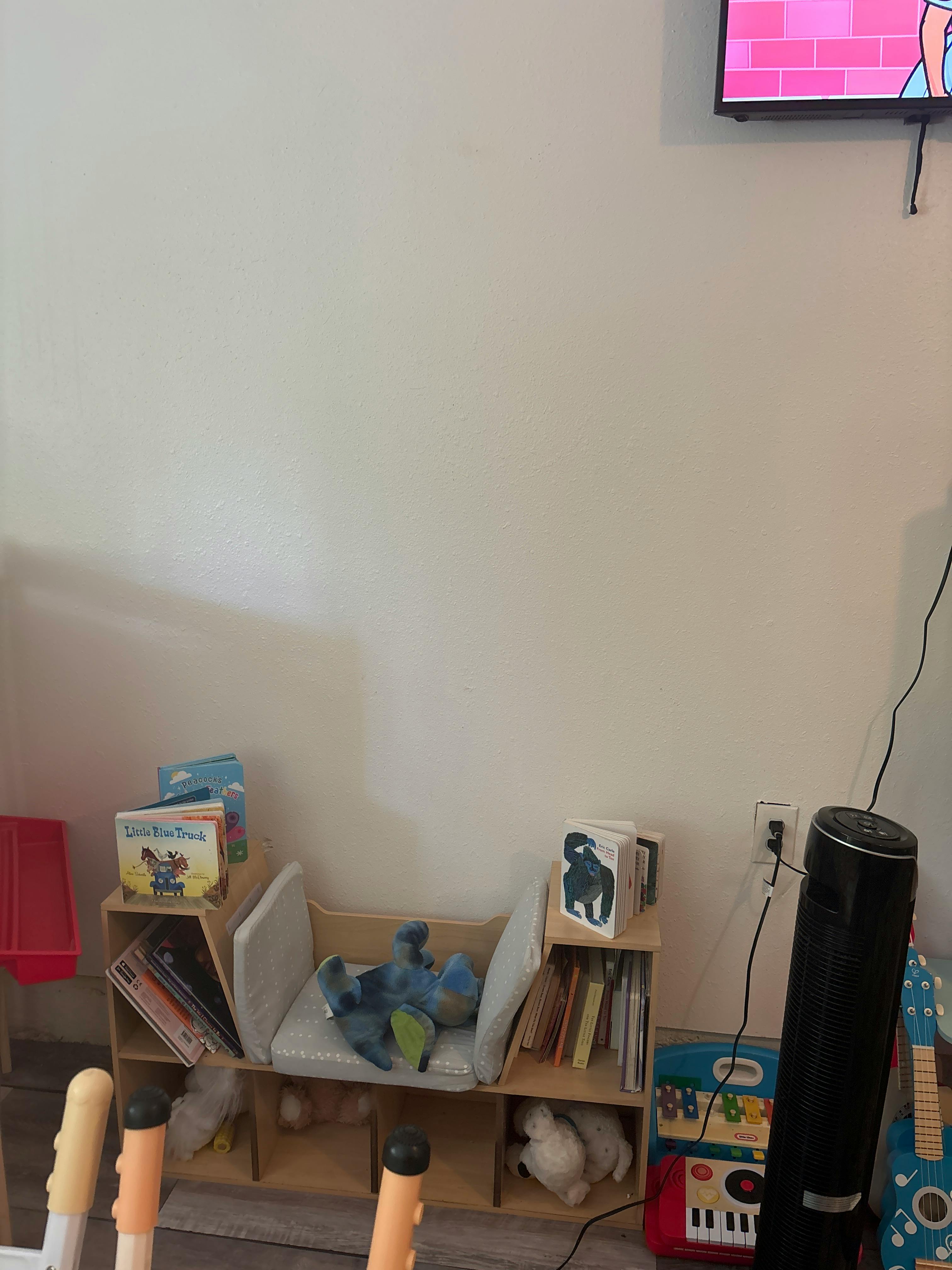 Bookshelf with books and stuffed animals, a fan, and a toy guitar