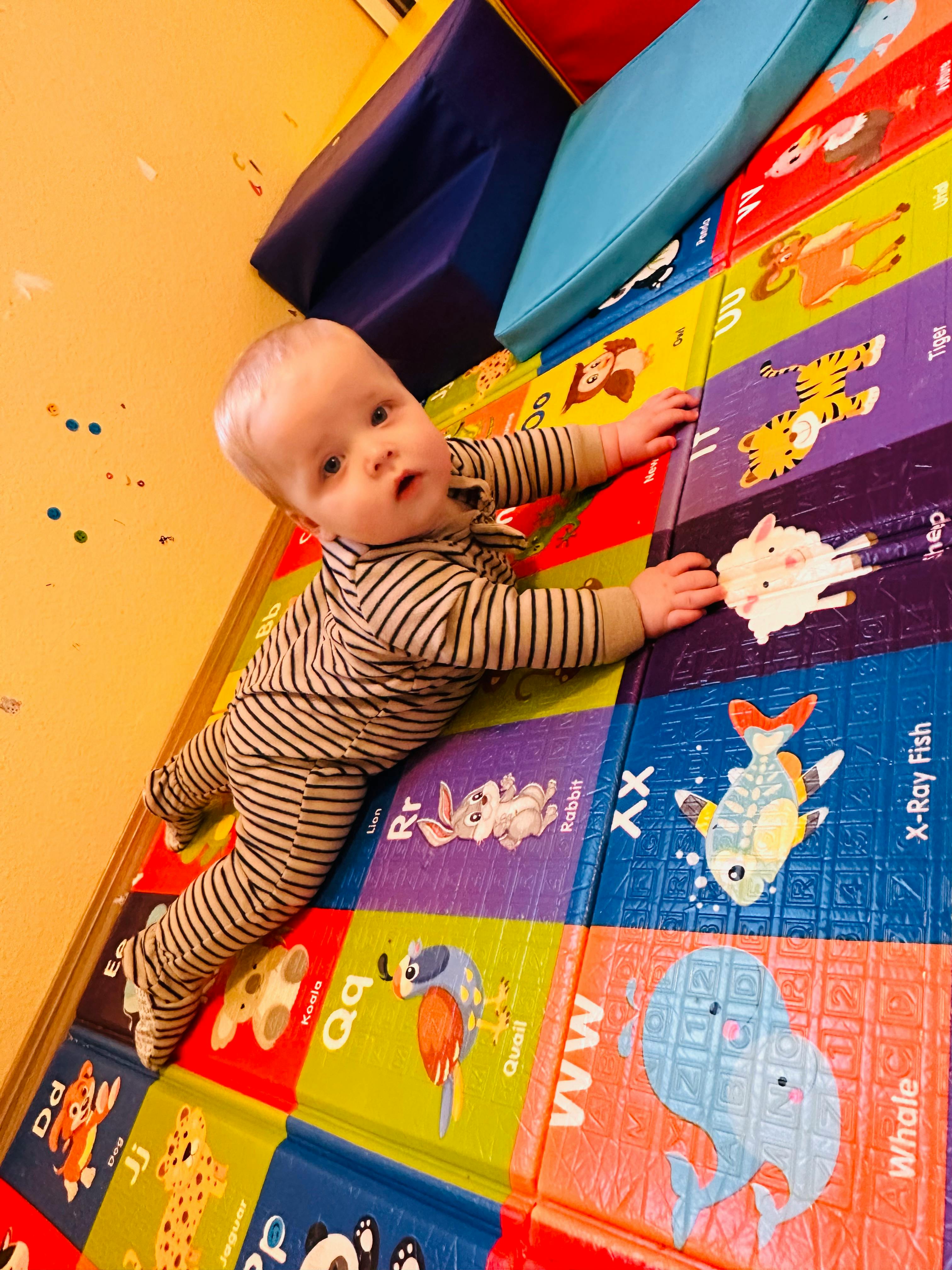 Baby in striped pajamas crawling on a colorful alphabet playmat