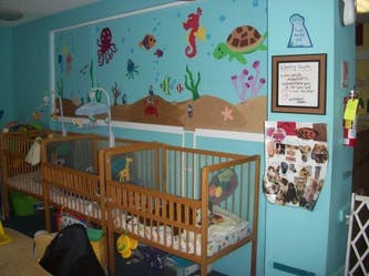 Two cribs in a room with an ocean-themed mural
