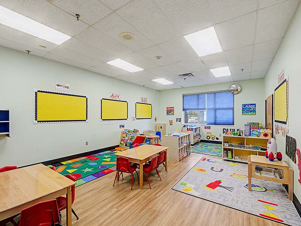 Empty classroom with small tables and chairs, and bulletin boards
