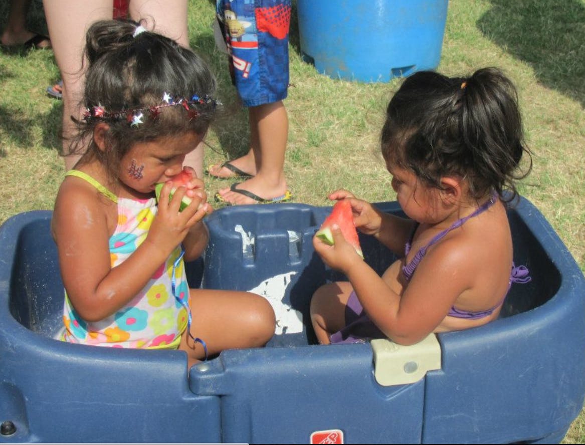 Two children eating watermelon in a blue plastic tub