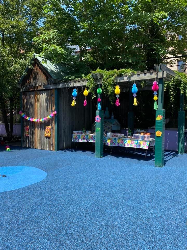 Outdoor play area with blue ground, wooden shed, and decorated canopy