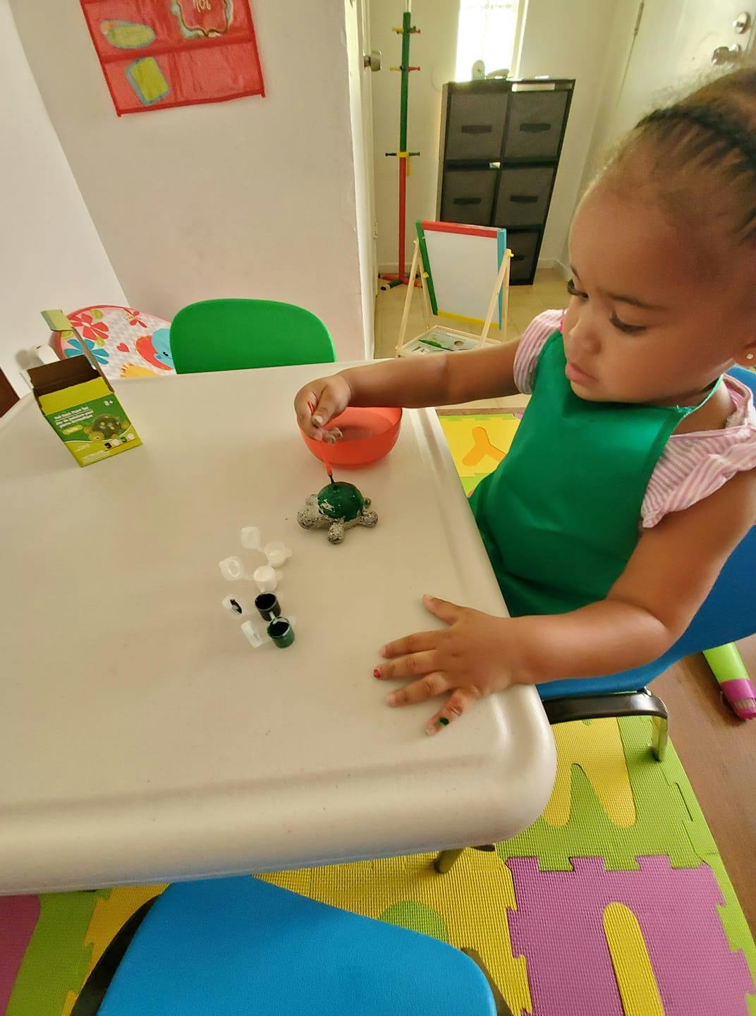 Child in a green bib playing with small objects at a table
