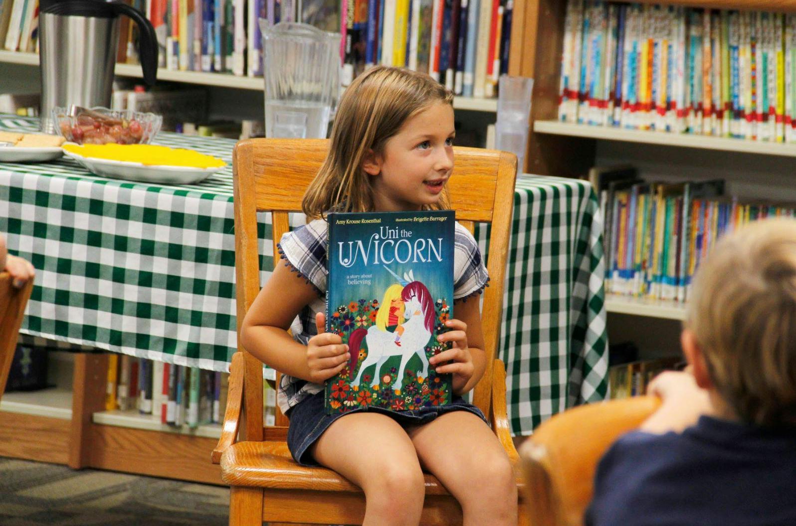 Child sitting on a chair holding a book titled "I Am the Unicorn"