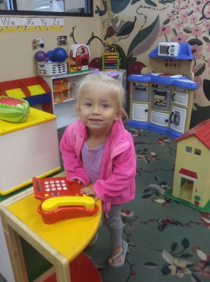 Child standing in a playroom with a toy phone