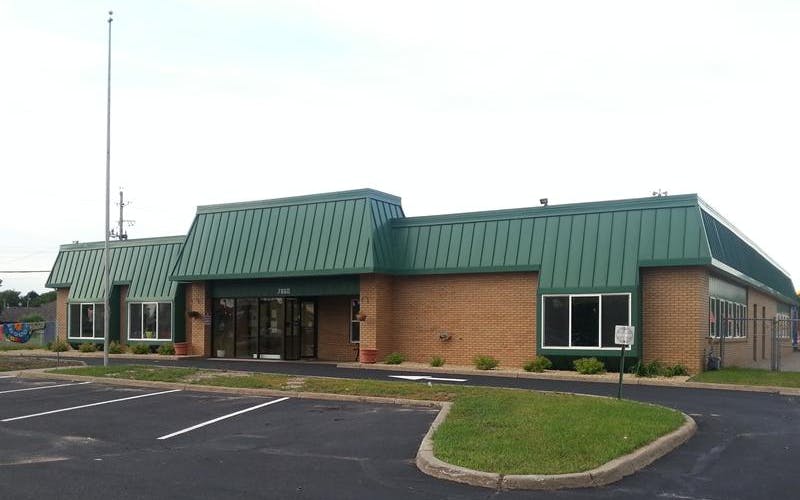 Brick building with a green roof, large windows, and a paved parking lot