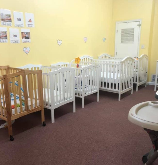 Multiple cribs in a room with yellow walls