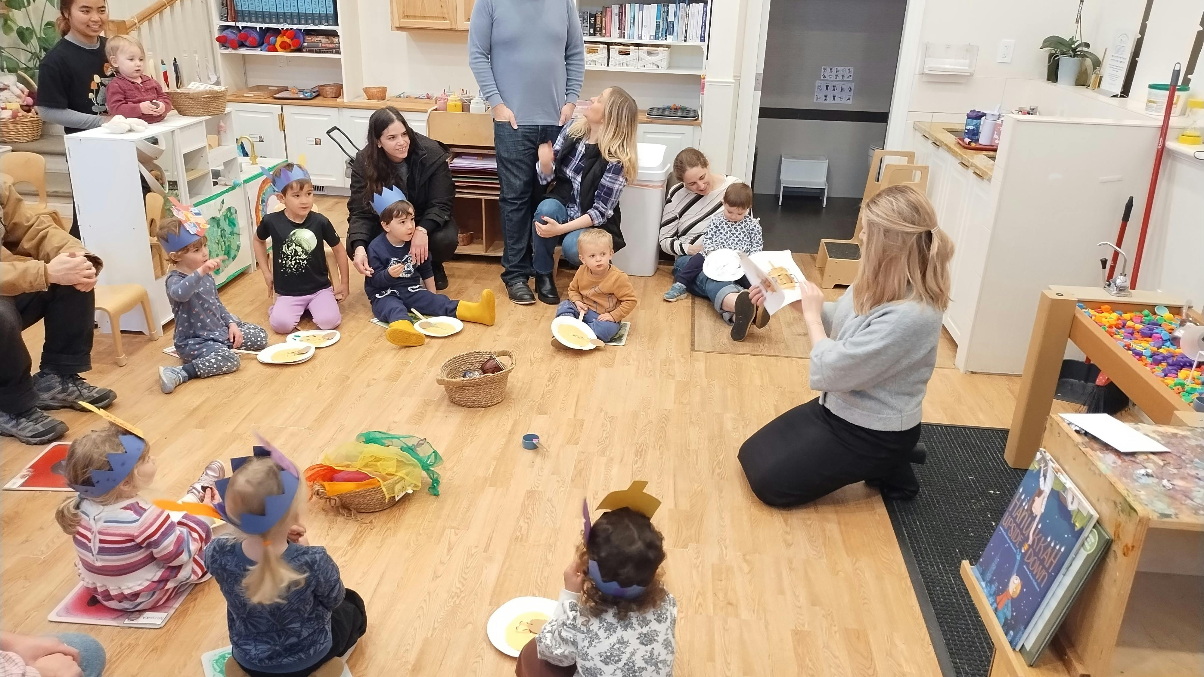 Adults and children gathered on a wooden floor in a classroom