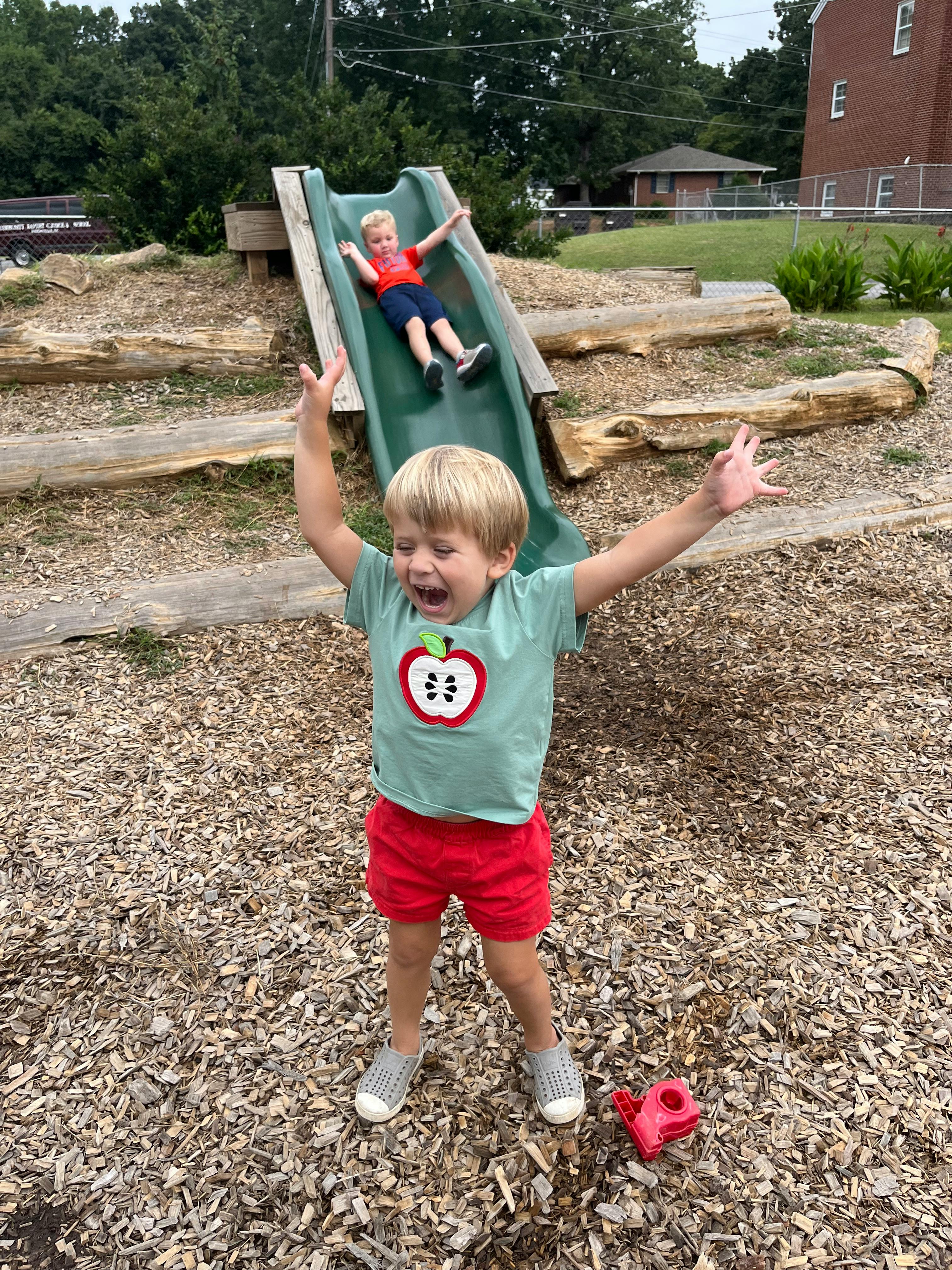 Child on a slide and another child standing with arms raised on a playground