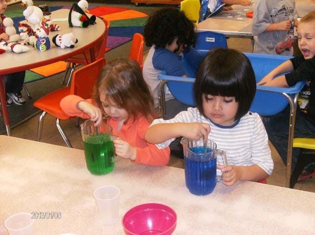 Two children stirring colorful liquids in a classroom