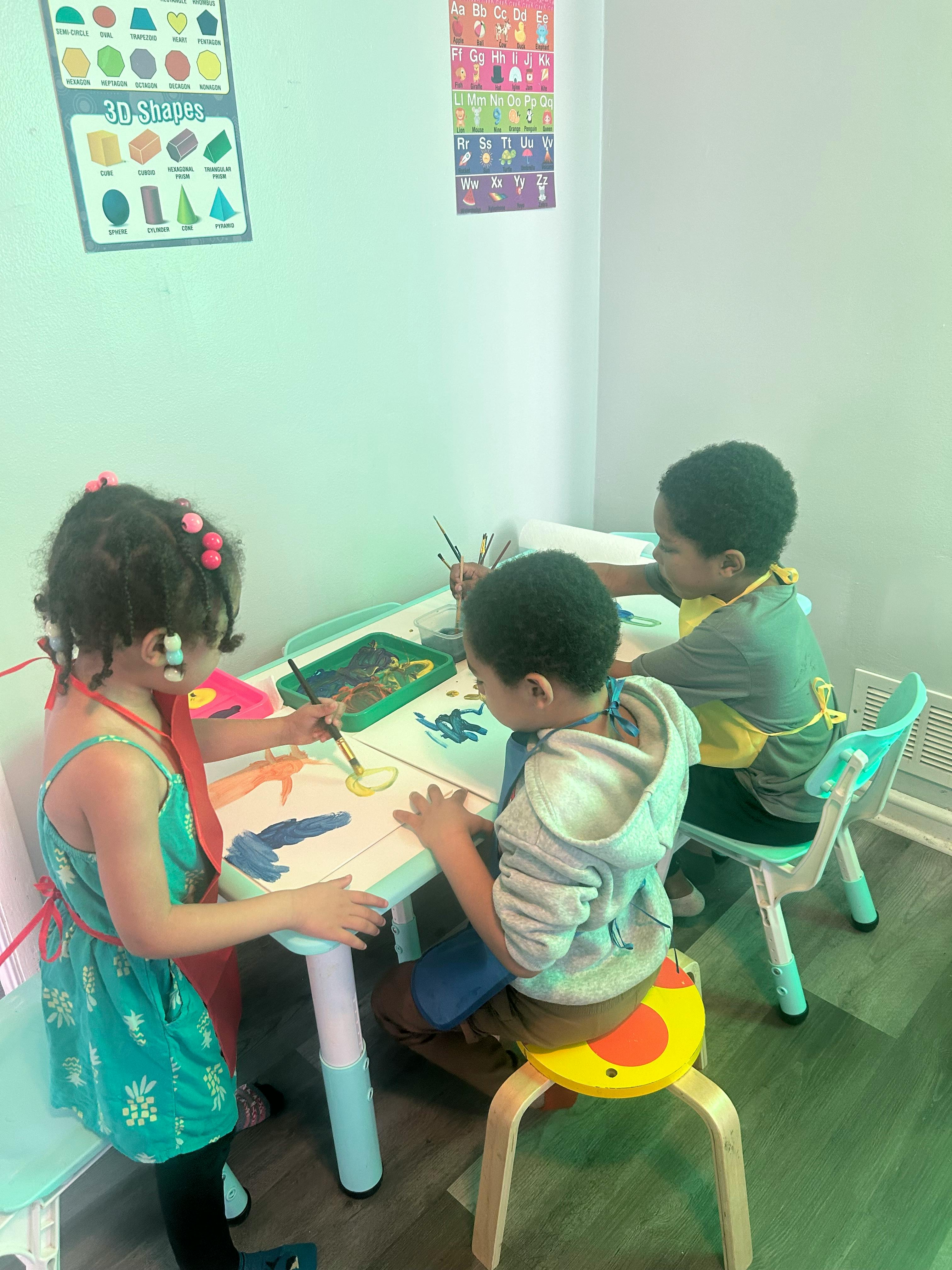 Three children painting at a table in a classroom