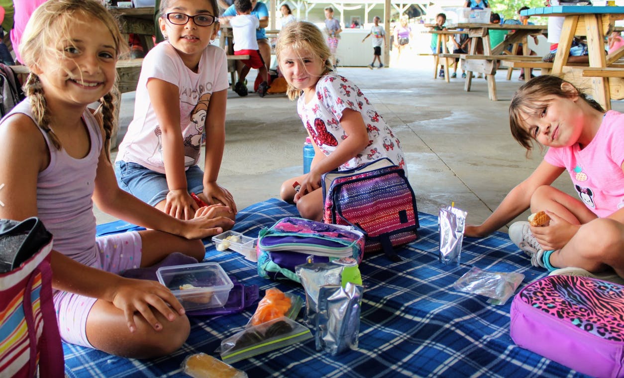 Four children sitting on a blanket with lunch items