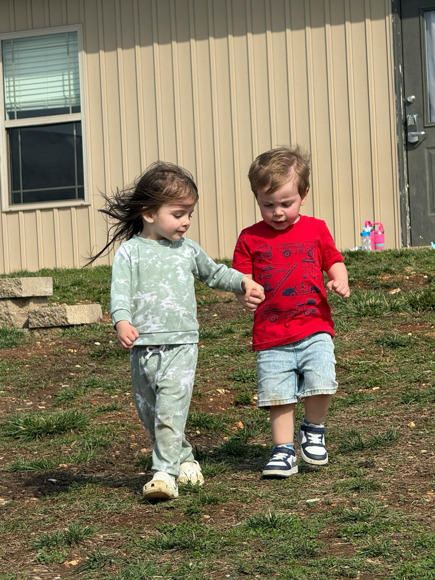 A child holding the hand of another child while walking on grass