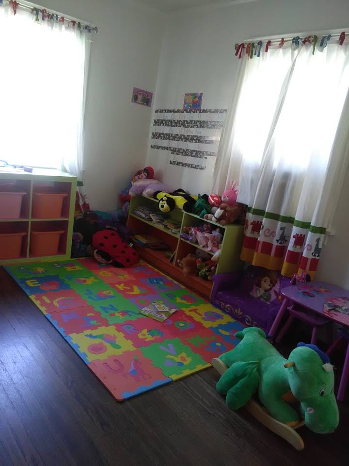 Playroom with colorful floor mat, shelves of toys, and windows