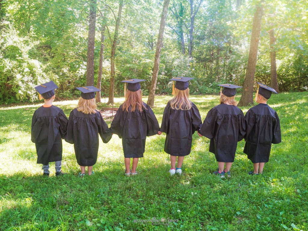 Children in graduation caps and gowns holding hands
