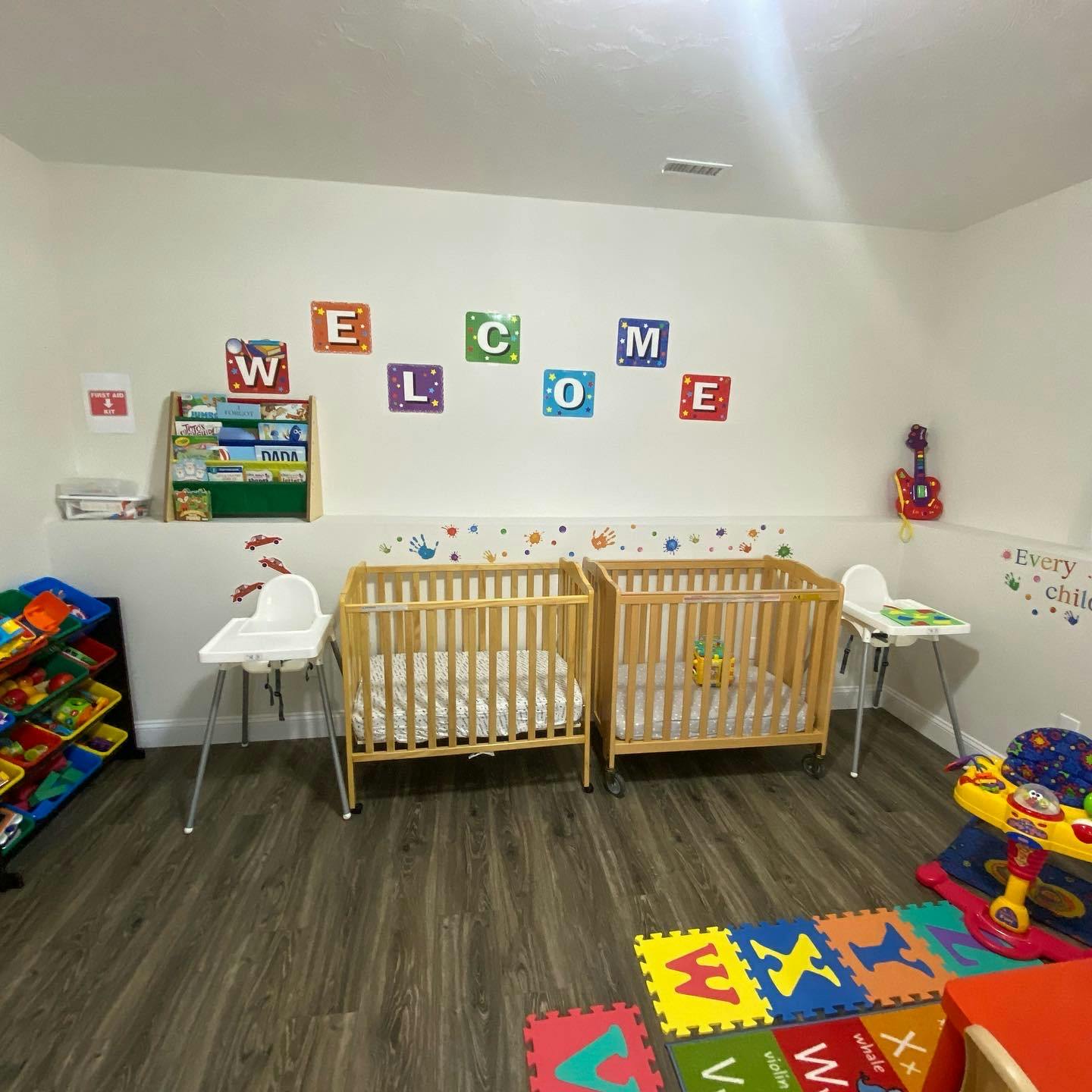 Two cribs and high chairs in a room with colorful wall decorations