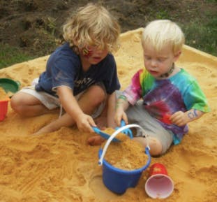 Two children playing in a sandbox with toys
