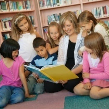 Adult and multiple children reading a book together in a library