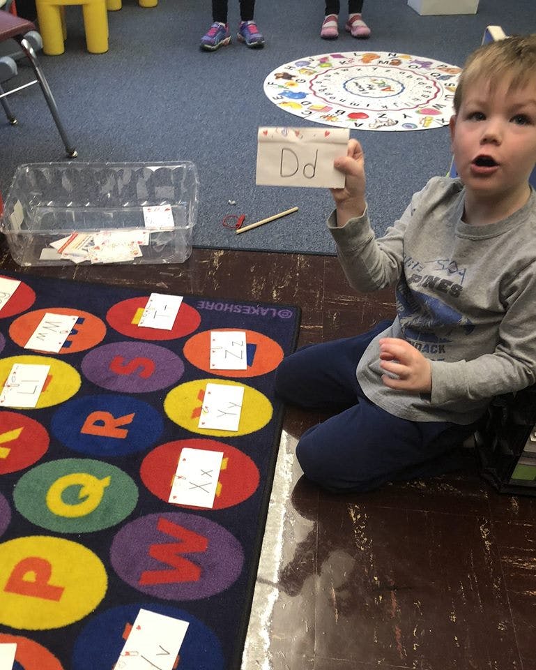 Child holding up a card with the letter Dd in a classroom