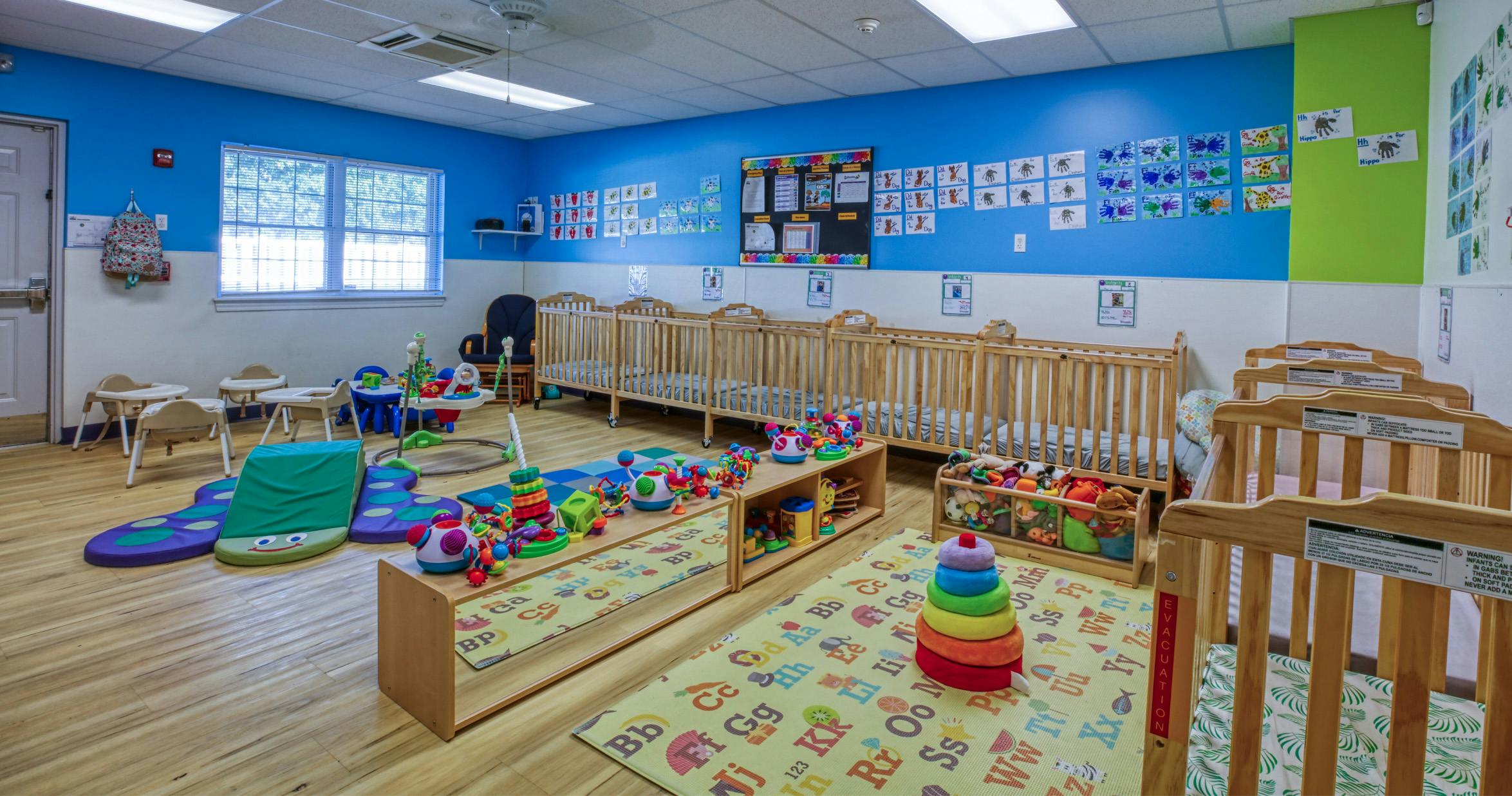 cribs, high chairs, and children's toys in a daycare room