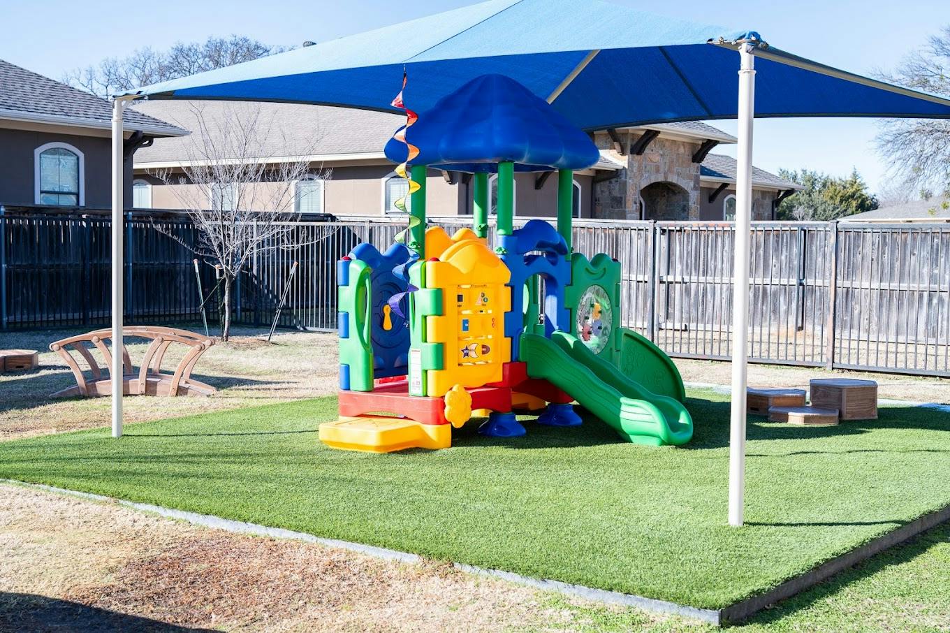 Colorful playground structure on artificial turf under a blue shade canopy