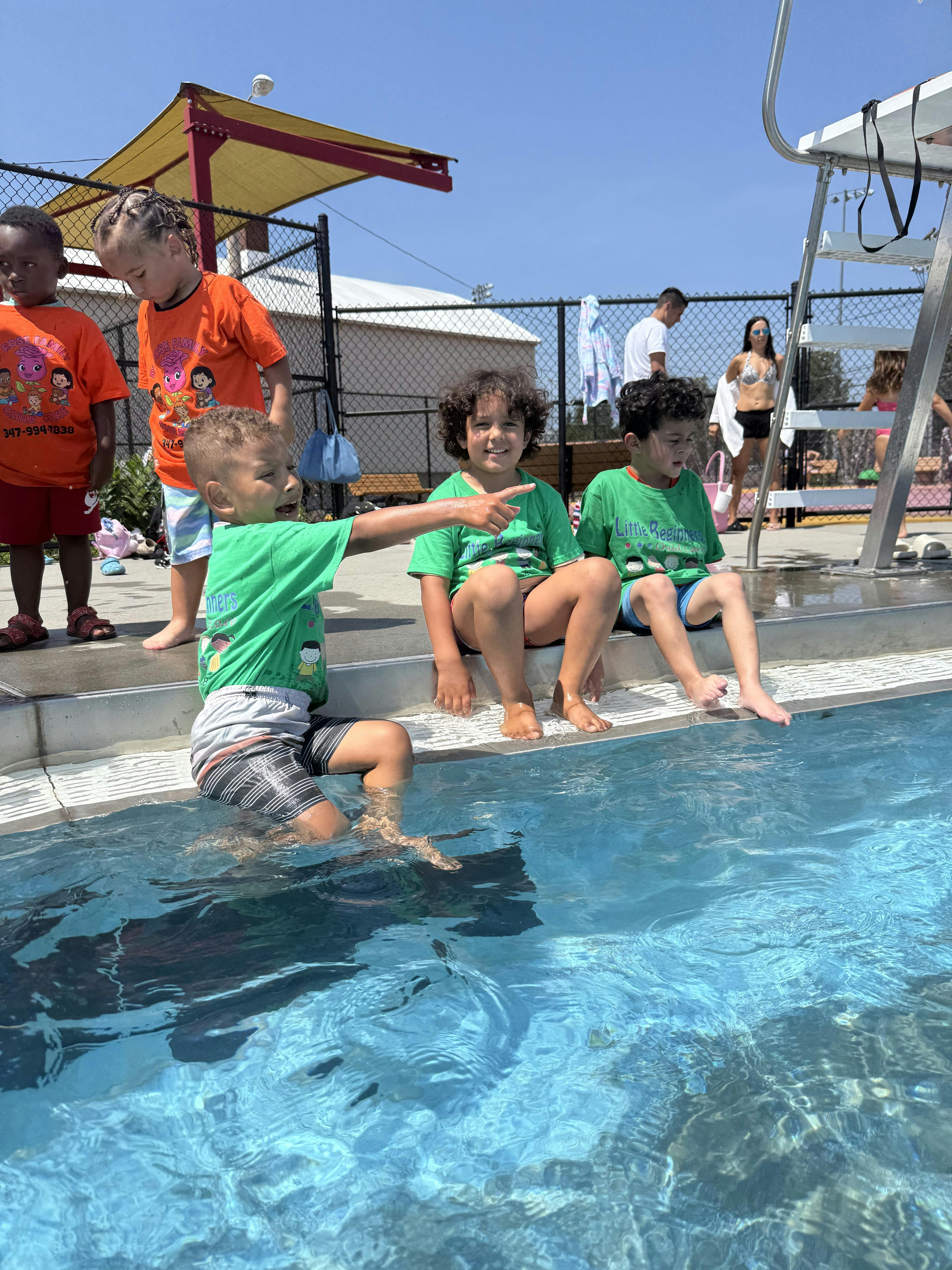 Children sitting on the edge of a swimming pool with one child pointing