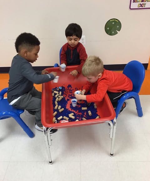Three children playing at a red sensory table in a classroom