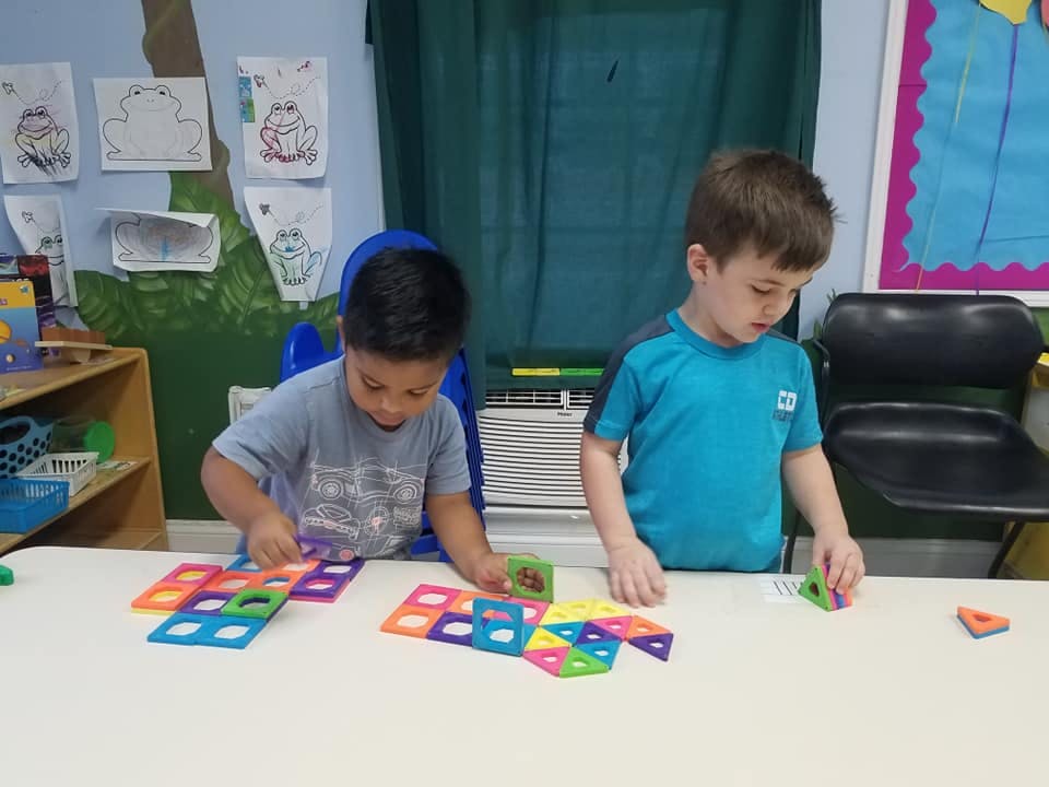 Two children playing with colorful magnetic tiles at a table