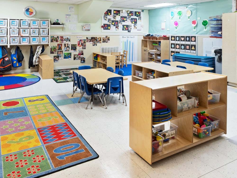 Empty colorful preschool classroom with small tables, chairs, and learning materials