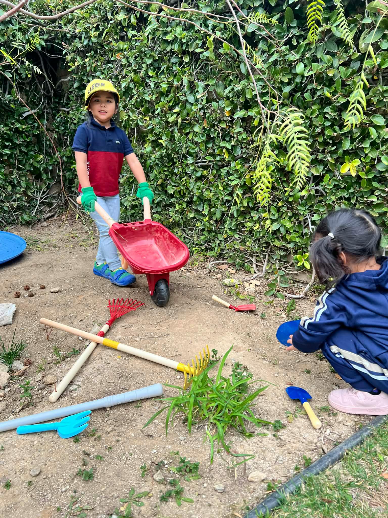 Two children playing with toy gardening tools in a garden