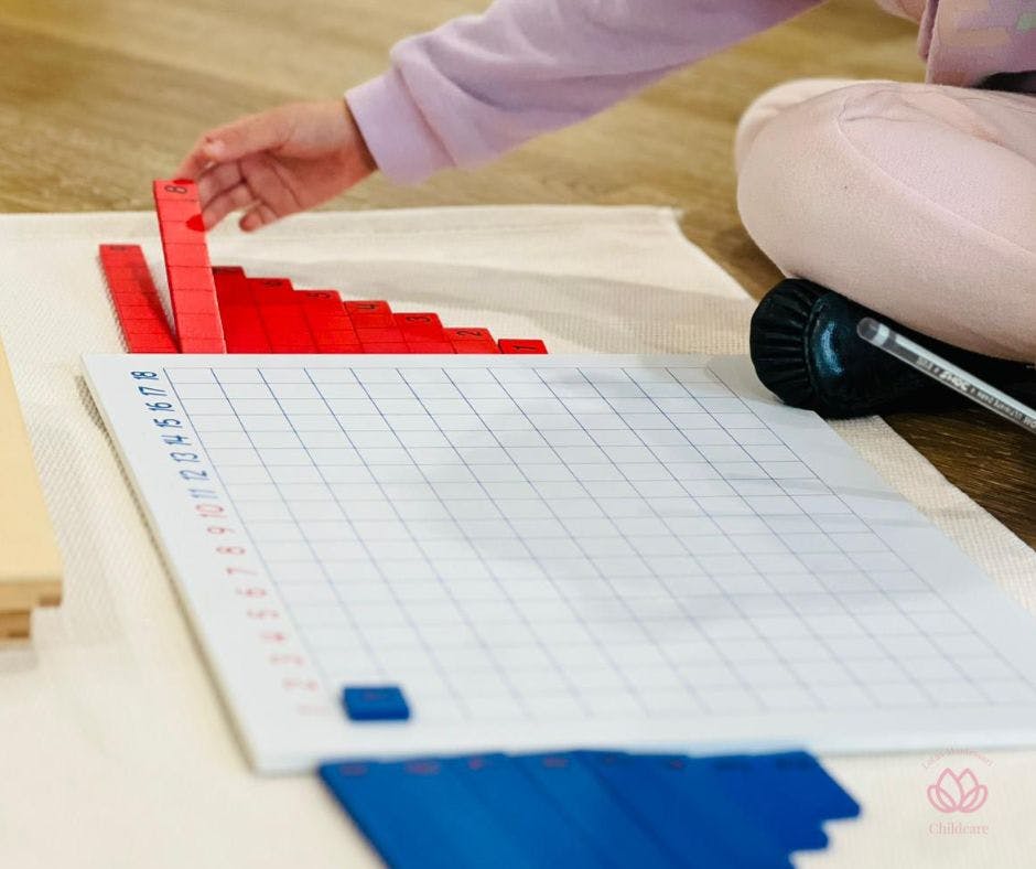 Person arranging red blocks on a mat with a grid