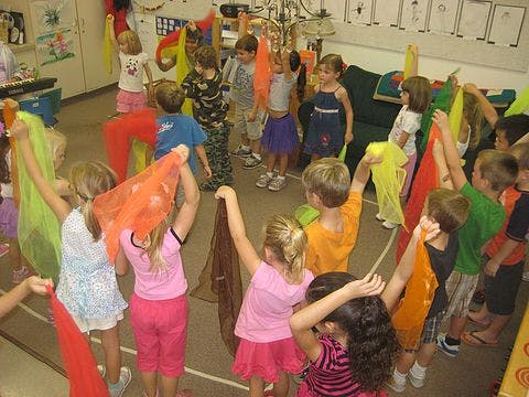 Children holding up colorful scarves in a classroom