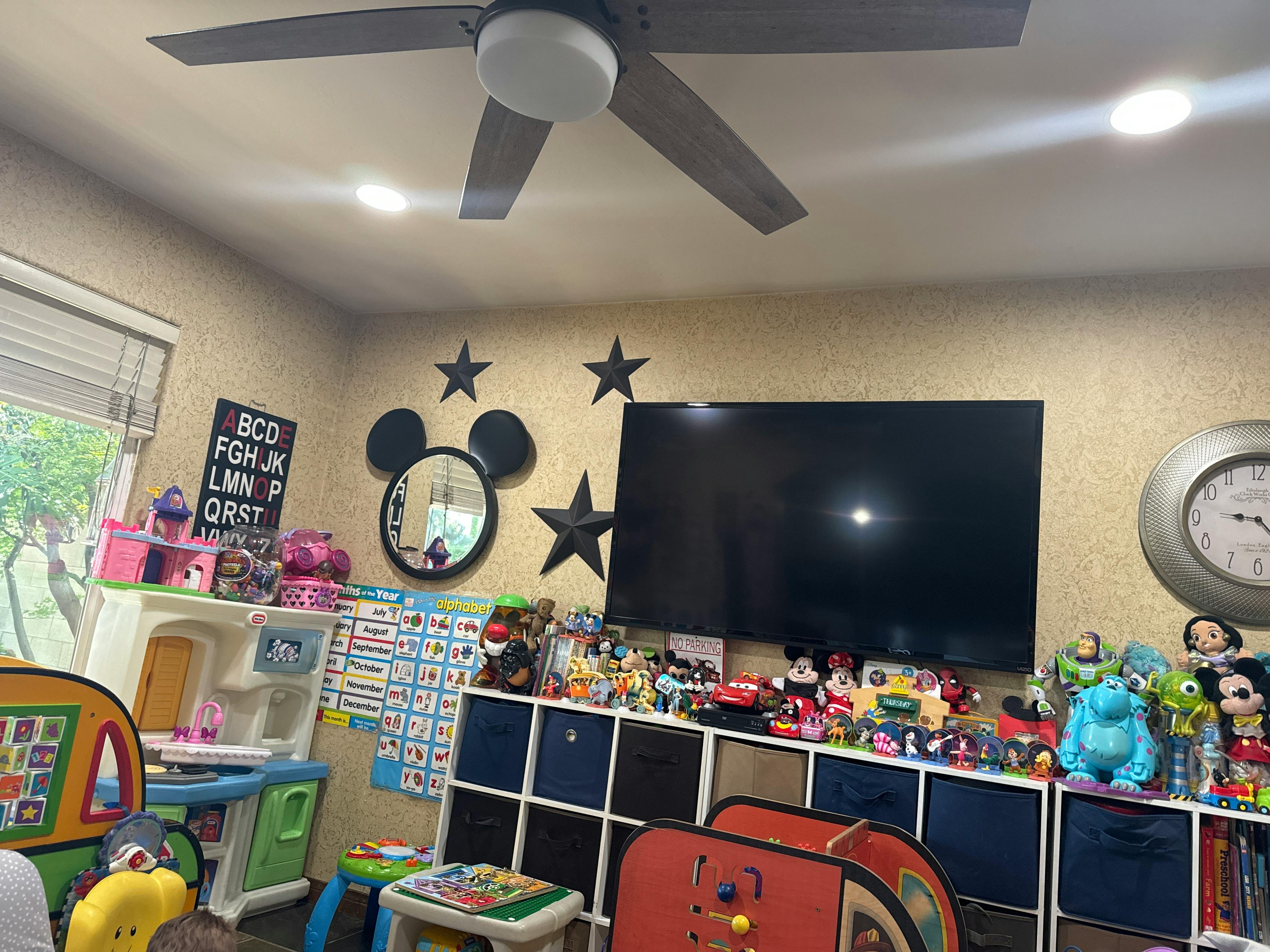 Room with a ceiling fan, television, and shelves filled with toys