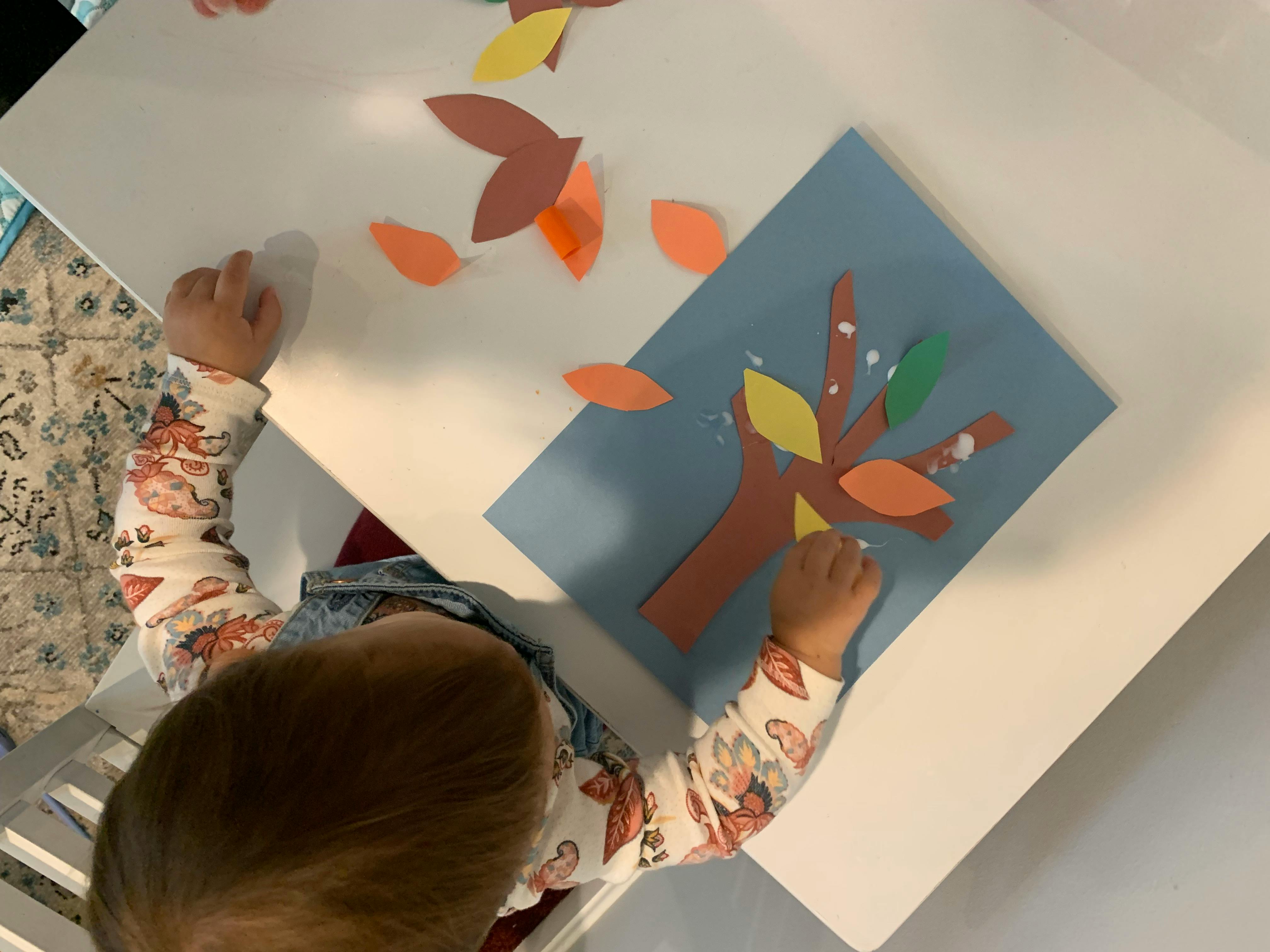 Child gluing paper leaves onto a paper tree cutout