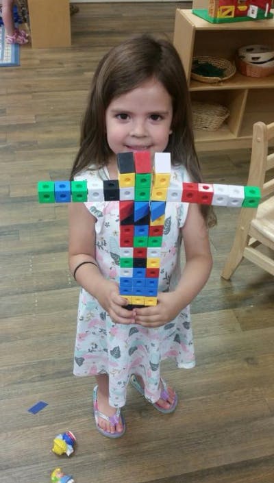 Child holding a large construction made of colorful interlocking blocks