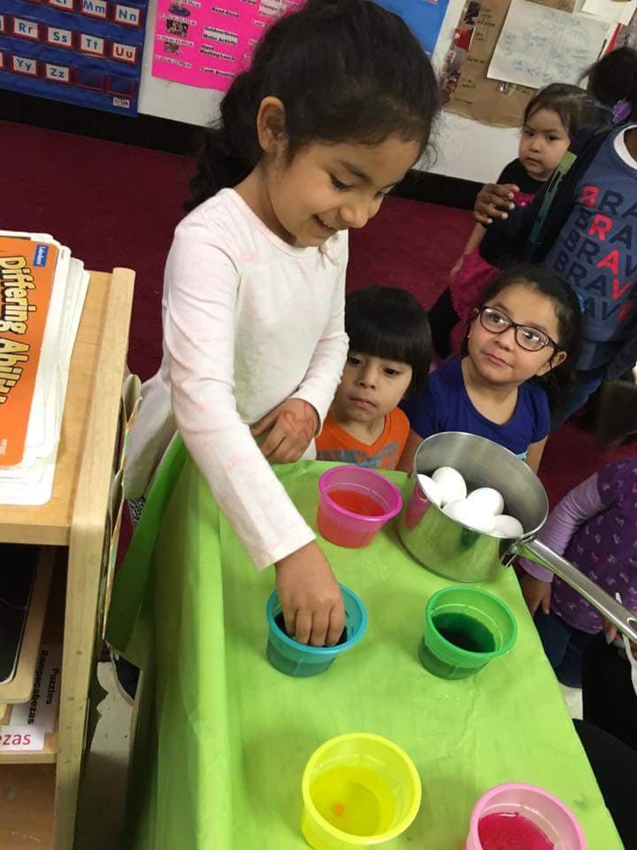 Child dipping an egg into a cup of colored liquid