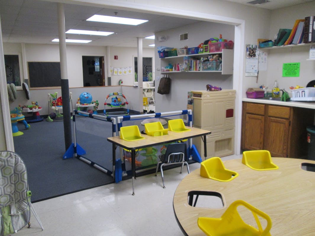Childcare room with play area and small tables with yellow chairs