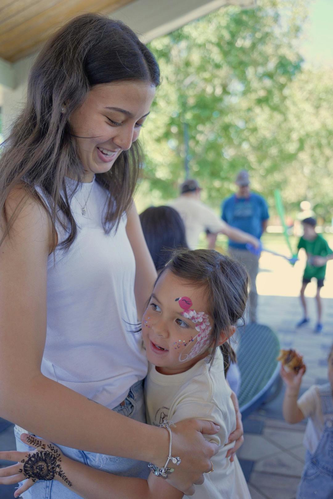 A person holding a child with flamingo face paint