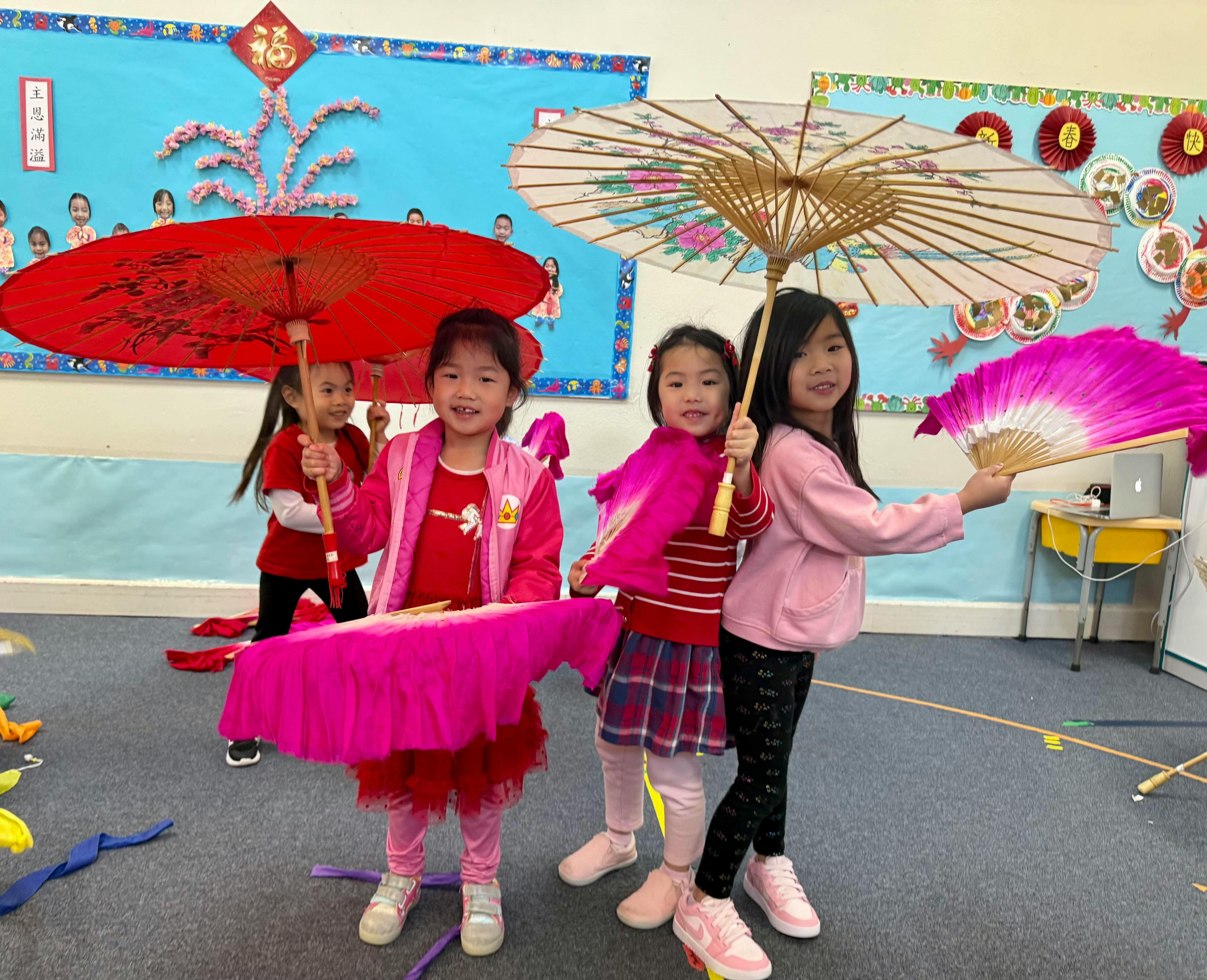 Children holding umbrellas and fans in a classroom