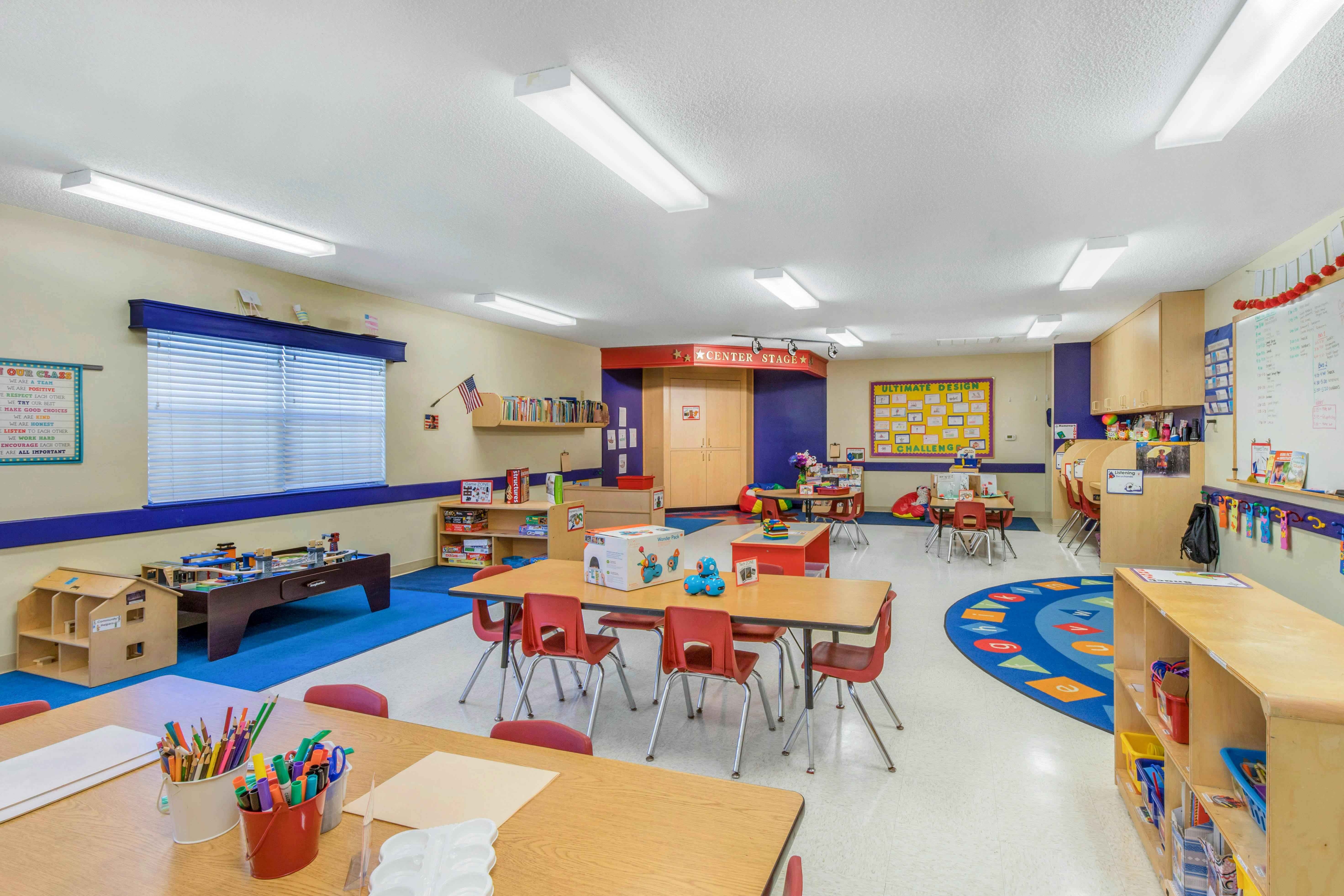 Classroom with tables, chairs, learning materials, and an alphabet rug