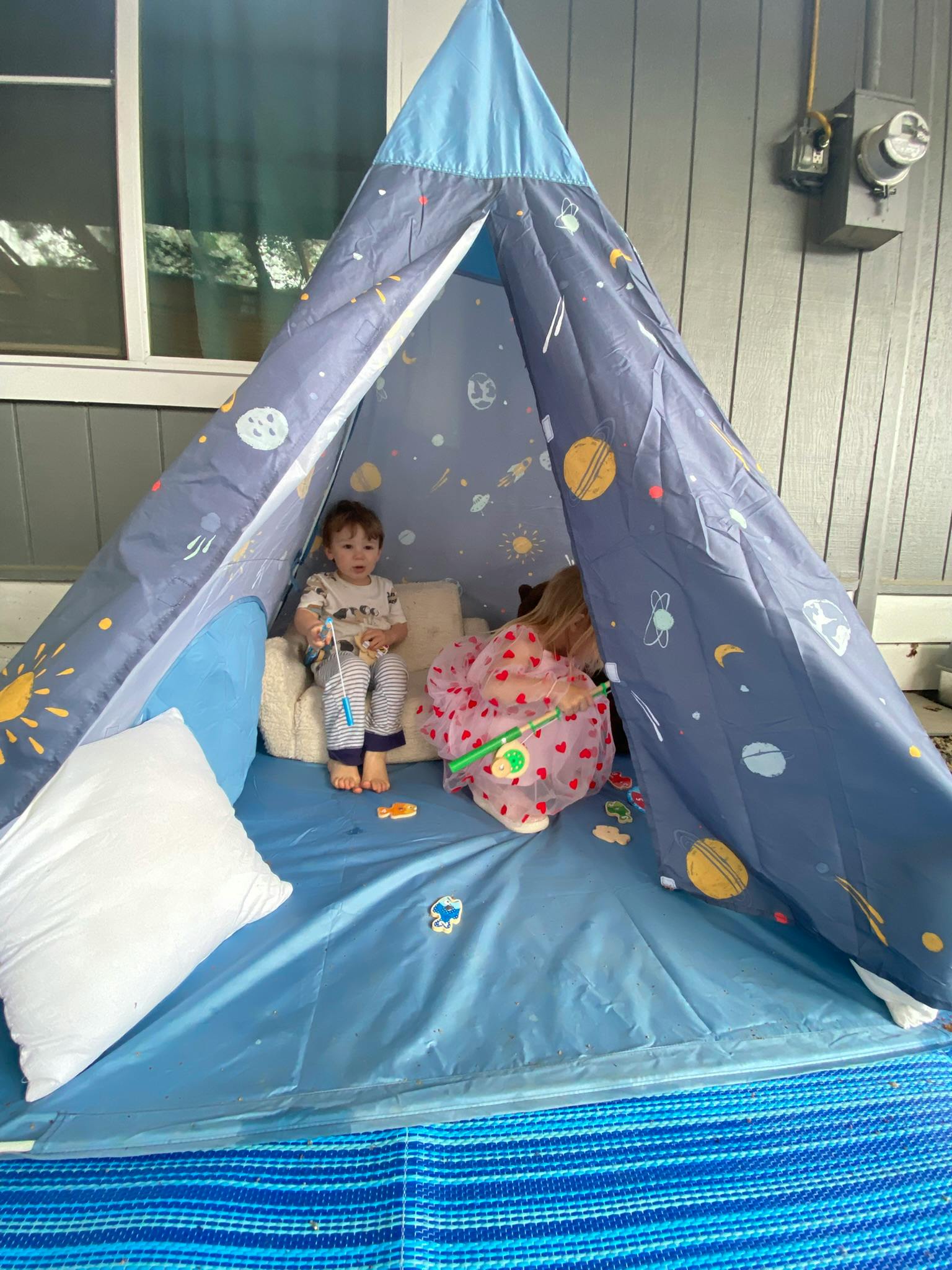 two children playing inside a blue tent decorated with planets