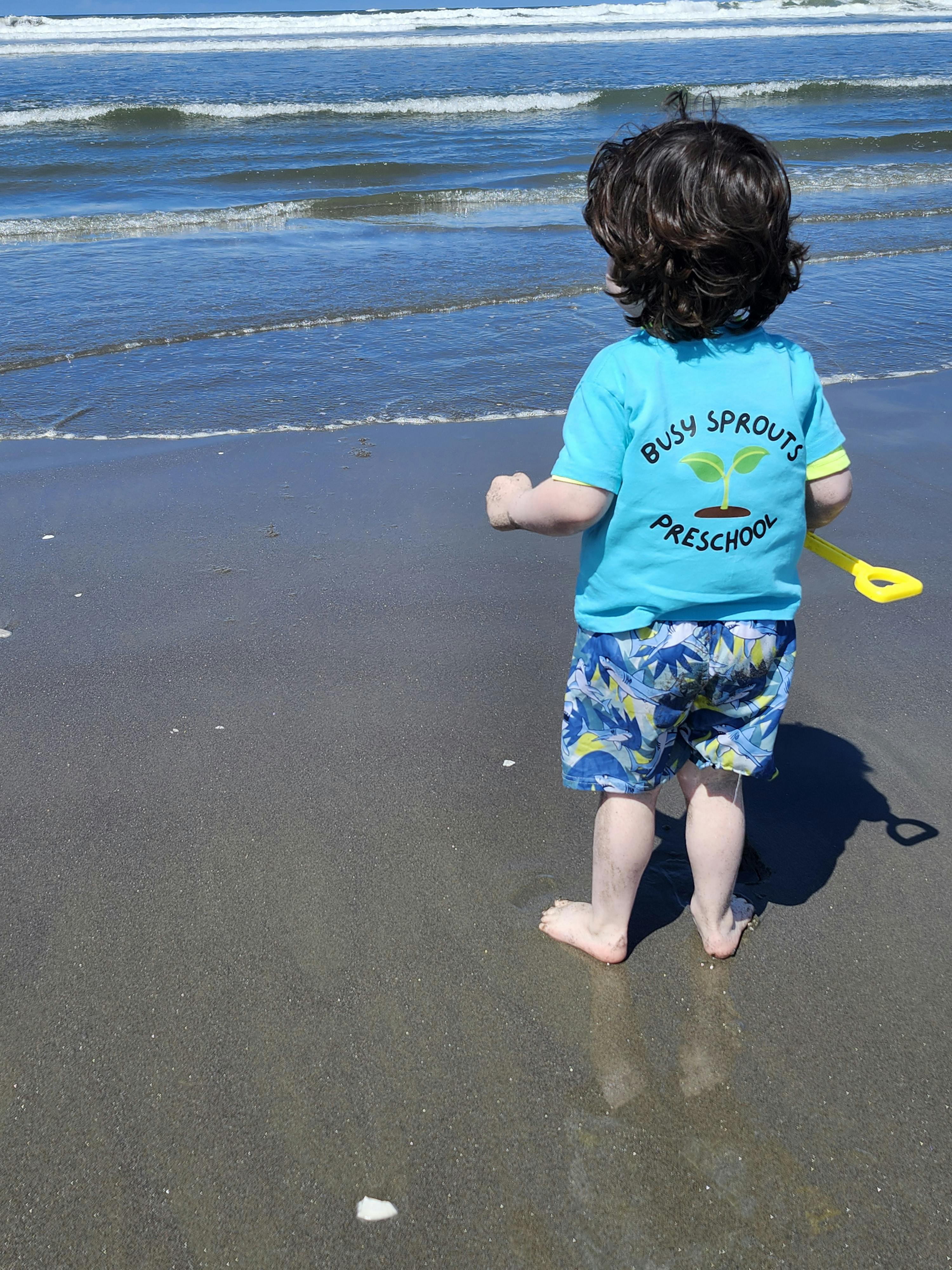 Child wearing a Busy Sprouts Preschool shirt walking on a beach