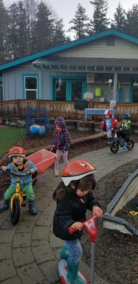 Children playing with bikes, a scooter, and a wheelbarrow outdoors