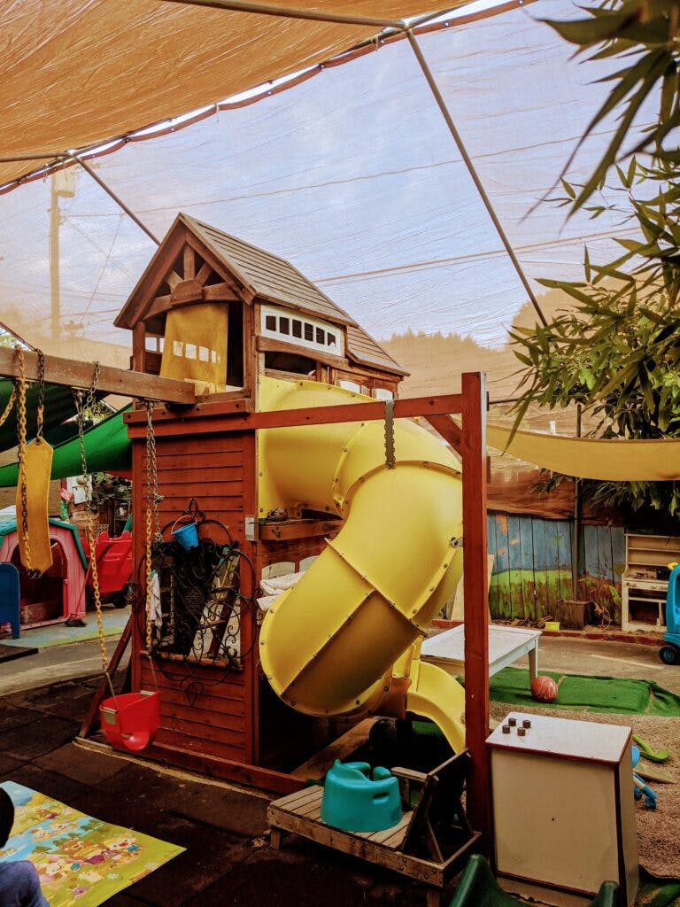 Wooden playhouse with a yellow tube slide and swings