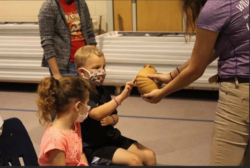 Person handing an object to a child wearing a mask, another child nearby